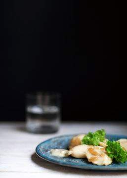 Vareniki on a ceramic plate and a black background with a salad