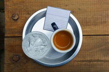 ristreto of espresso coffee in dark blue cup with sparkling water in transparent glass in the round aluminium plate on the wooden table.