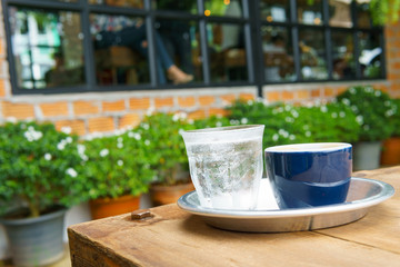 ristreto of espresso coffee in dark blue cup with sparkling water in transparent glass in the round aluminium plate on the wooden table.