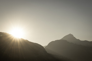 Farewell to the day. Sun with bright rays against a clear blue sky. Sunset at the top of the mountains. Mourning filling