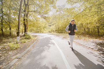Young smiling sporty man running in park in the morning. Fitness man jogging in park.