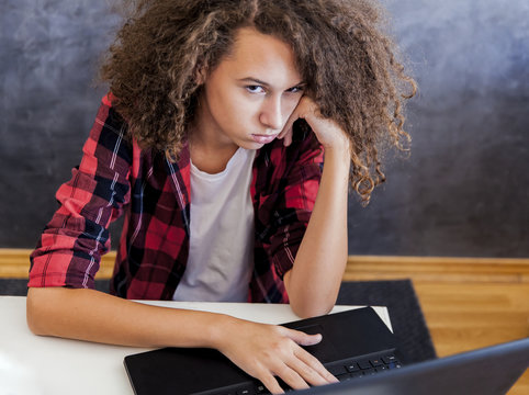 Unhappy teenage girl using laptop at h ome