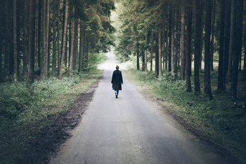 Naklejka premium young blonde caucasian woman walking on narrow road through dark forest