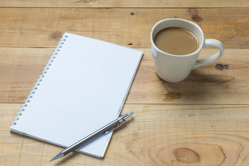 Open notebook with cup of coffee on wooden