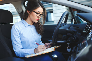 Beautiful young business woman sitting in the car looking at her planner.