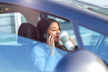 Young business woman sitting in the car drinking coffee and talking at phone.