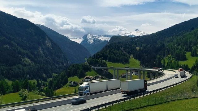 Aerial Shot of the Road  with Heavy Traffic Stretching into the Valley With Enormous Mountains With Snowpeaks in the Background. Shot on a Camera in 4K (UHD).