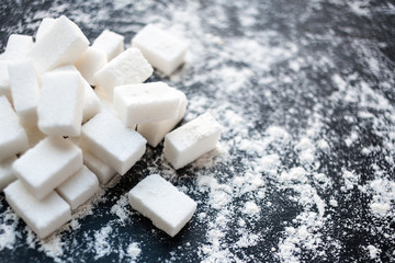 Unhealthy food concept - sugar  and flour on a black background. Dangerous high amount of sugar in food. Carbohydrates sources, top view.