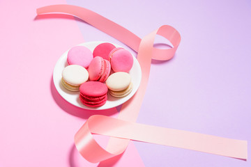 Homemade Colorful macaroons or macaron on White plate with copyspace on pink and purple background