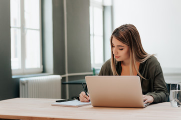 Blonde girl in library writing in notebook.