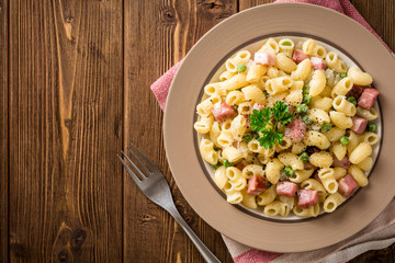 Pasta with green peas, onion, bacon and cheese on wooden background
