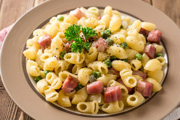 Pasta with green peas, onion, bacon and cheese on wooden background