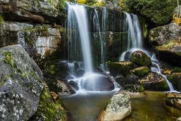 Waterfall falling on stones through autumn forest. Fall nature specification.
