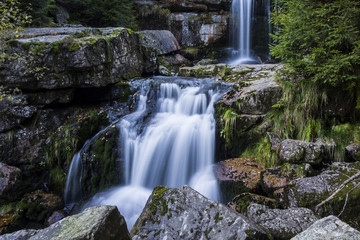 Fototapeta na wymiar Waterfall falling on stones through autumn forest. Fall nature specification.