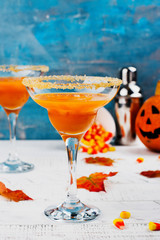 Autumn pumpkin margarita cocktail with halloween decor on wooden table. Copy space