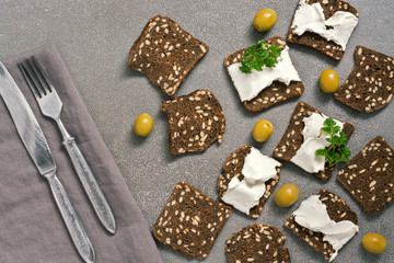 Italian crackers with seasonings and cheese are decorated with olives on a gray surface, top view.