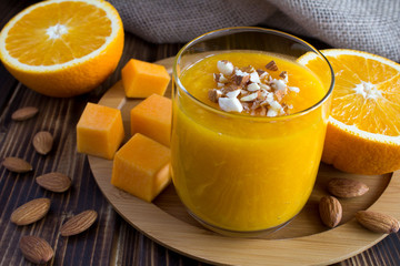Smoothie with pumpkin, orange and almond on the round wooden cutting board