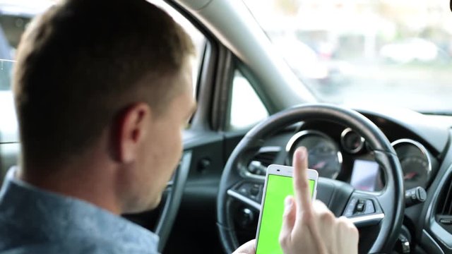 man in the car uses a smartphone with a green screen.