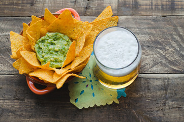 Nachos with guacamole and beer on rustic wooden background.