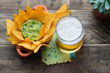 Nachos with guacamole and beer on rustic wooden background.