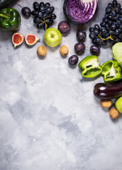 Fresh organic raw green and purple colored vegetables and fruits on stone background. Top view.