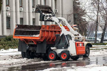 loading snow into a truck on a city street in winter