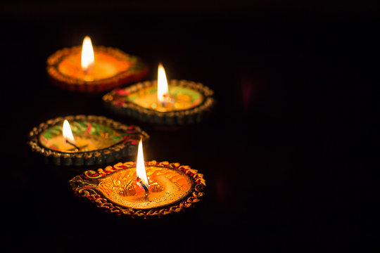 Four burning colorful clay diya lamp Diwali celebration. Black background. Selective focus.