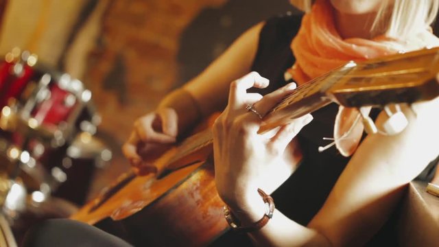 Blond hair young beautiful girl plays music by acoustic guitar in summer cafe close-up