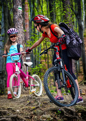 Fototapeta premium Bikes cycling family. Happy mother and daughter wearing helmet are cycling on bicycles into forest. Parenting. Children travel unaccompanied.