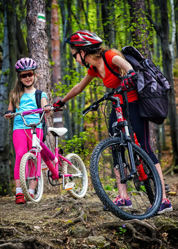 Bikes cycling family. Happy mother and daughter wearing helmet are cycling on bicycles into forest. Parenting. Children travel unaccompanied.