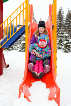 Girl with little sister slide down the hill on the Playground in winter