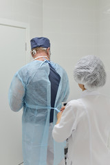 Fototapeta na wymiar Surgery, assistant helps surgeon to put on surgical clothes, back view .