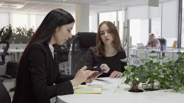 Woman boss is showing something to her employee on the screen of a smartphone during the meeting
