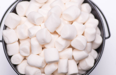 White mini puffy marshmallows ia a black bowl on white background with copy spase. Top view, close-up.
