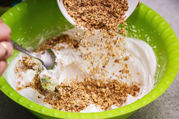 Milled walnut is poured in a bowl with sour cream. It is shown the process of preparing a sweet cream for a cake at home