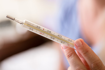 Close-up of hand holding analog medical thermometer for checking temperature