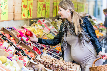 Pregnant woman shopping groceries on farmers market choosing