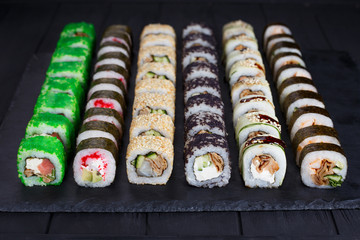 Delicious appetizing set of traditional uramaki and futomaki sushi rolls with wide assortment of fillings on black stone slate, close up
