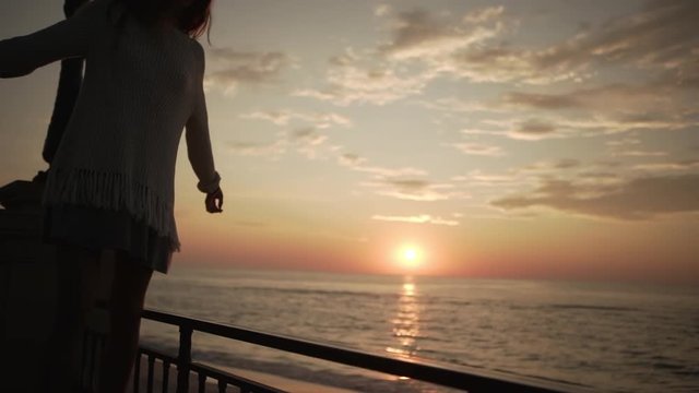 in slow motion silhouette of skinny long-haired girl walking along parapet of embankment keeping balance looking far into sea on amazing sunset