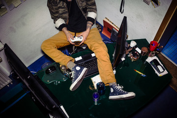 Cropped high-angle view of a teenager with video game addiction playing on computer, with a game controller while sitting on a messy desk at home © Kzenon