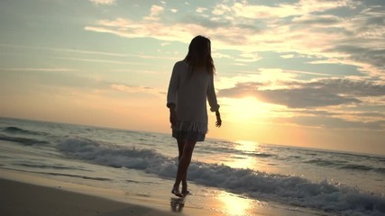 happy long-haired girl running on water along empty beach feeling free while water washing over her feet leaving footprints on wet sand at colourful dawn slow motion
