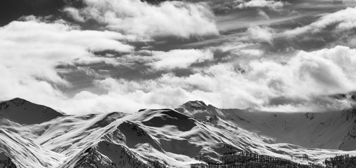 Black and white panoramic view on snow sunlight mountains and cloudy sky in sun evening