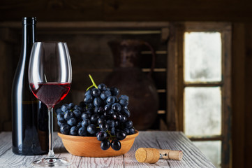 Still life of red wine with wooden keg. Wine bottle, glass of red wine and grape on a old wooden barrel. Wine tasting and production concept.