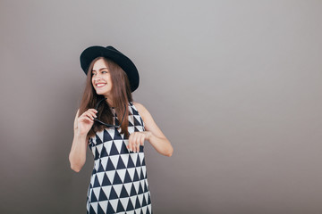 Young beautiful fashionable woman with trendy makeup  in black hat and glasses on the grey background . Model looking at camera, wearing stylish eyeglasses. Female fashion, beauty concept. 
