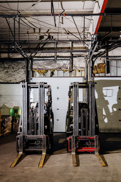 Two forklifts sitting side by side in a warehouse.