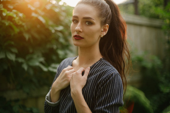 Female in overgrown alleyway at sunset in long sleeve pinstripe dress