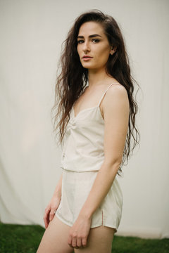 Pretty female model with long dark curly hair and cream romper with a septum piercing