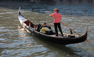 Gondola and gondolier in Venice / A typical and iconic image of Venice, Italy, a Gondolier leads his gondola with two tourists on a beautiful sunny day