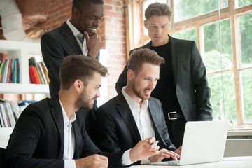 Multiethnic team of corporate employees looking at laptop screen. Businessman typing on computer screen, african american colleague smiling. Group of coworkers browsing new investment opportunities.