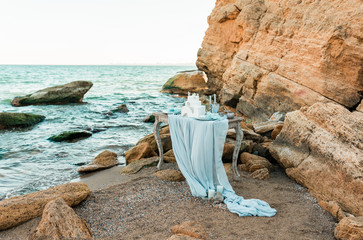 Luxury decorated table and wedding cake for a romantic date. Wedding details: candles, seashells, sea stones on a sand of beach with wave on background